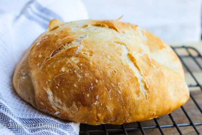 This Homemade Dutch Oven Crusty Bread tastes like the fresh bread straight from the best bakery. But it comes from your oven and it only takes 10 minutes of prep time. There is no kneading involved! Homemade Dutch Oven Crusty Bread on a rack and towel