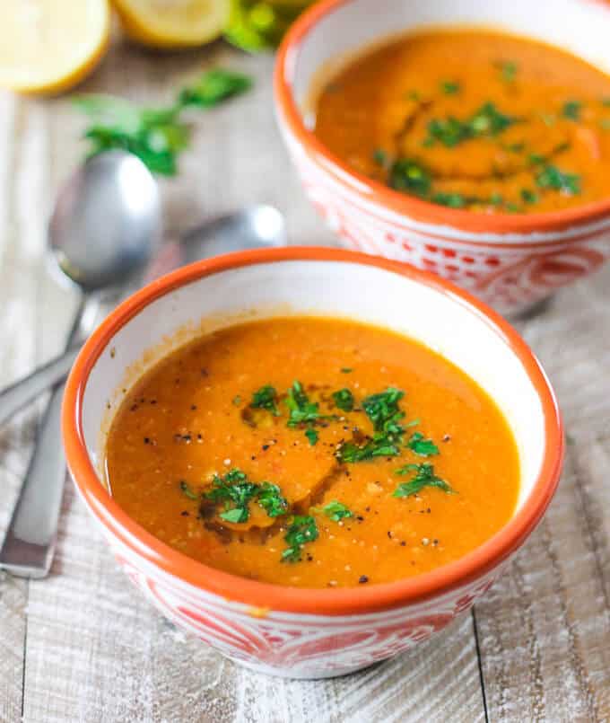Perfect healthy, vegan, gluten free treat on chilly fall or freezing cold winter days. Tomatoes Red Lentils Coconut Soup - doesn't it sound amazing? Two bowls of Tomatoes Red Lentils Coconut Soup with spoons on a side
