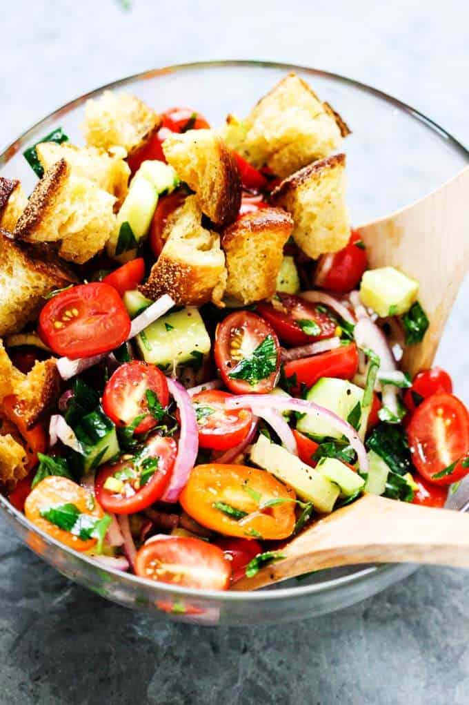 This popular Italian salad is a perfect addition to any summer meal or BBQ. Crusty bread that's been infused with garlic butter makes this it irresistible. Next time if you're looking for a perfect side dish try this amazing Summer Panzanella with Garlic Butter Bread. Panzanella Salad in a glass bowl with two wooden spoons.