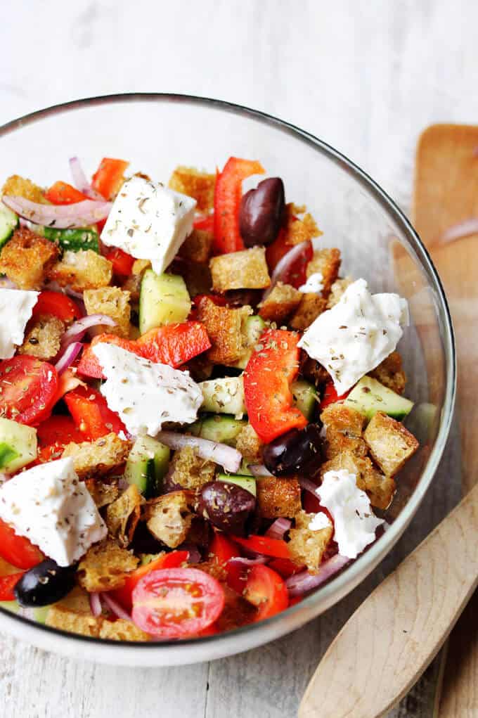 Greek Panzanella Salad combines traditional Greek salad flavors, like Kalamata olives, and tangy feta with bread cubes toasted in tasty garlicky vinaigrette. Greek salad with bread cubes in a bowl;