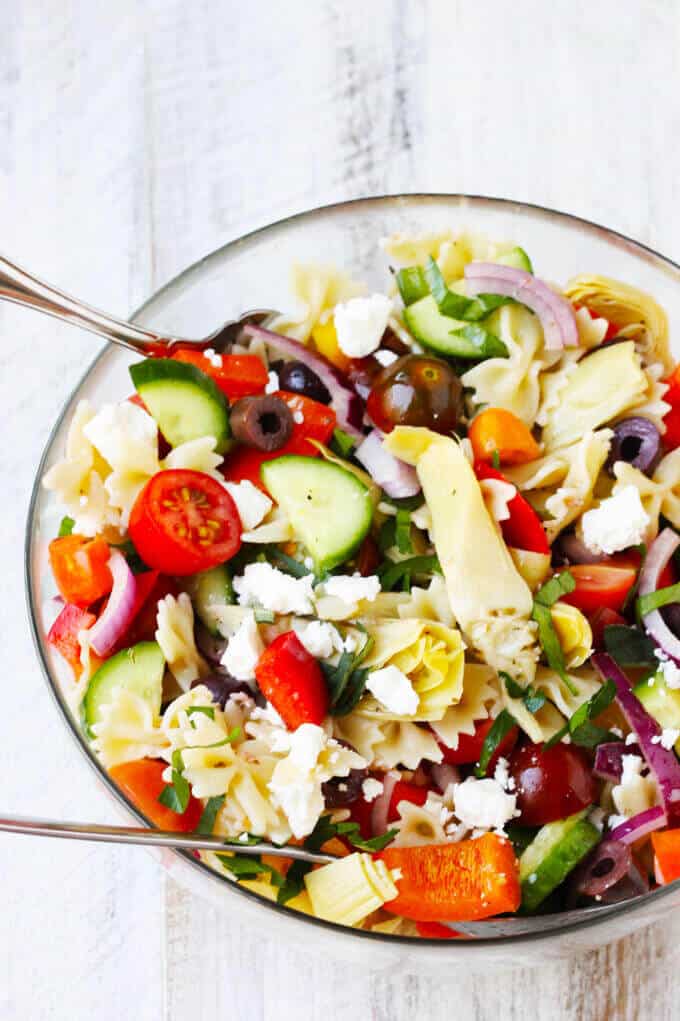 Farfalle Pasta Salad Mediterranean Style is a great bow tie pasta salad with super fresh ingredients like cucumbers, tomatoes, onions, and peppers. Kalamata Olives, marinated artichokes and feta cheese, combine to enhance those Mediterranean flavors. Dressed with a red wine based vinaigrette, instead of mayo, makes for super light and refreshing spin on a classic. Bow tie pasta salad with Mediterranean twist with veggies, olives, feta and no-mayo dressing