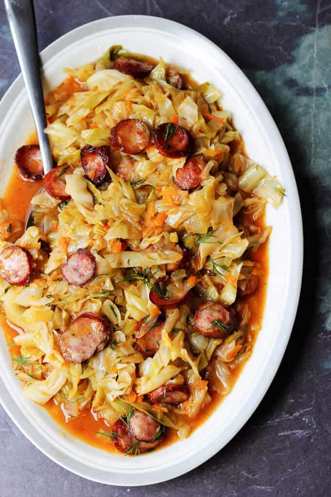 Kielbasa and Cabbage come together to form a perfect Polish summer hunter's stew. It's made from young cabbage, that is at its peak at the begging of the summer, with the addition of a smoky Polish sausage and a fragrant dill. It makes for a delicious European treat. Kielbasa and Cabbage (Hunter's stew) on a serving plate with spoon