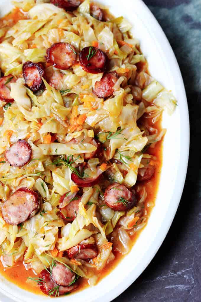Kielbasa and Cabbage come together to form a perfect Polish summer hunter's stew. It's made from young cabbage, that is at its peak at the begging of the summer, with the addition of a smoky Polish sausage and a fragrant dill. It makes for a delicious European treat. Summer hunter's stew with kielbasa and cabbage on a serving plate