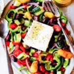 Horiatiki Greek Salad on a plate with jar of peppers on a side