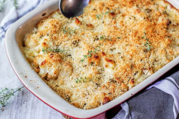 Cauliflower Pasta Bake with Brie and Fontina is like a combination of fancy mac & cheese with veggies! Two dishes at ones. Casserole of Cauliflower Pasta Bake with spoon and kitchen towel on a side