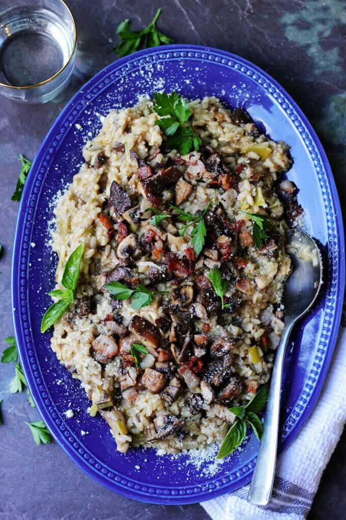 Wild Mushroom Risotto with Bacon and Leeks is exceptionally flavorful and delicious. Every bite introduces a combination of different flavors and textures. Mushroom Risotto with Bacon on a blue serving plate with spoon