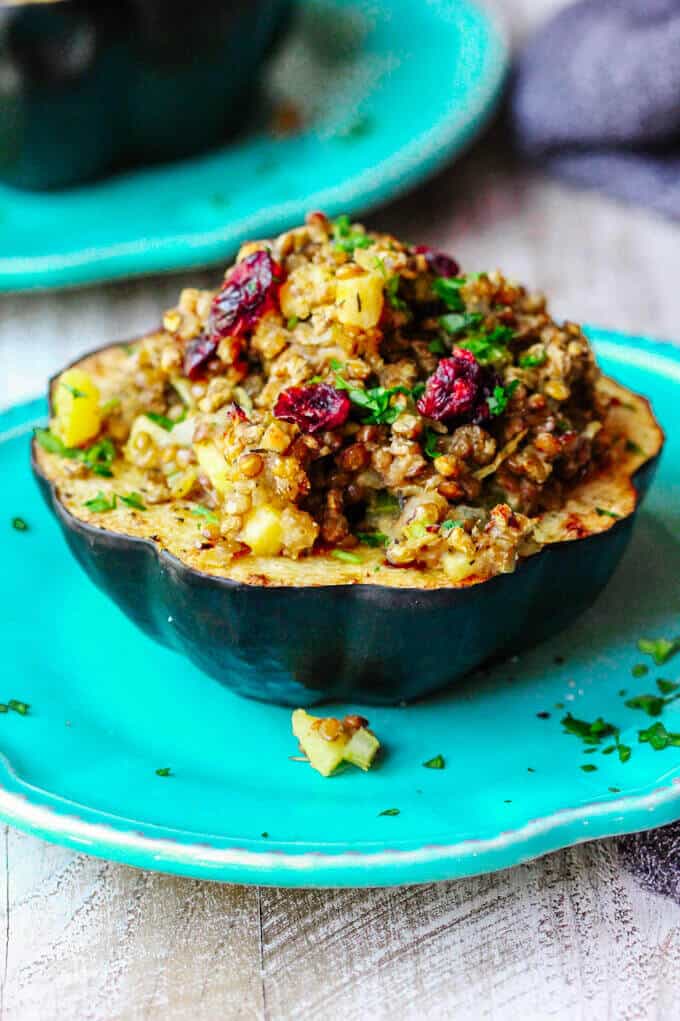 Lentils Stuffed Acorn Squash with apples, dried cranberries and thyme is a perfectly balanced vegetarian dish that combines all of your favourite fall flavors in every bite. Lentils Stuffed Acorn Squash with apples and dried cranberries on a blue plate
