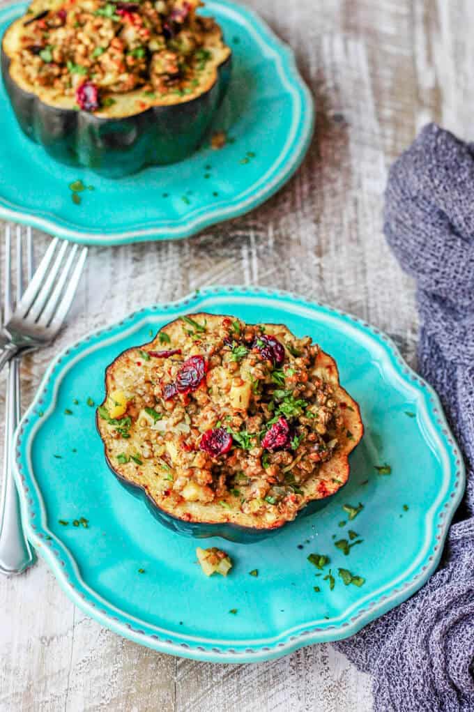Lentils Stuffed Acorn Squash with apples, dried cranberries and thyme is a perfectly balanced vegetarian dish that combines all of your favourite fall flavors in every bite. Two blue plates with lentils stuffed acorn squash