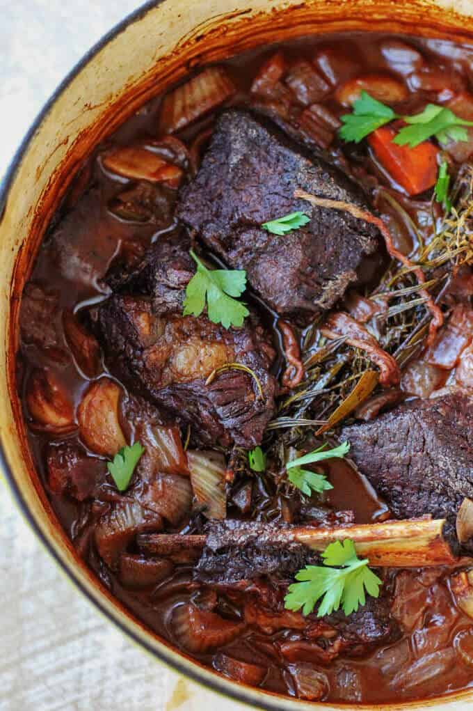 Red Wine Braised Short Ribs with Parmesan Polenta and Roasted Delicata Squash, is a super flavorful dinner idea that will make you feel warm and cozy on a cold, winter night. Red Wine Braised short ribs in a pot with vegetables and herbs