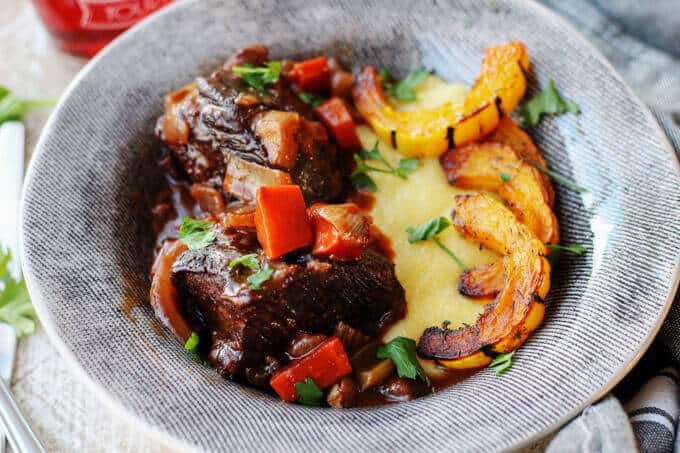 Red Wine Braised Short Ribs with Parmesan Polenta and Roasted Delicata Squash, is a super flavorful dinner idea that will make you feel warm and cozy on a cold, winter night. Braised short ribs with polenta and squash in a gray plate