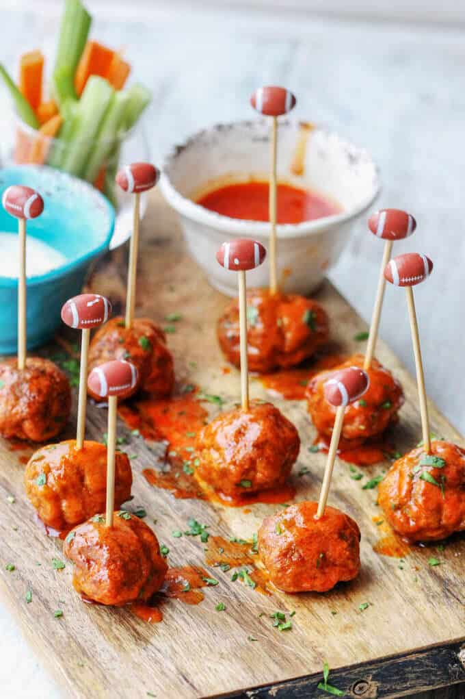Buffalo Turkey Meatballs are a perfect appetizer for the Big Game. They're also a lighter alternative to a traditional chicken buffalo wings, not only because they have less fat, but also because they're baked, not fried. Not to mention they're also super easy to make. Buffalo Turkey Meatballs with football sticks and hot sauce and blue cheese on a side