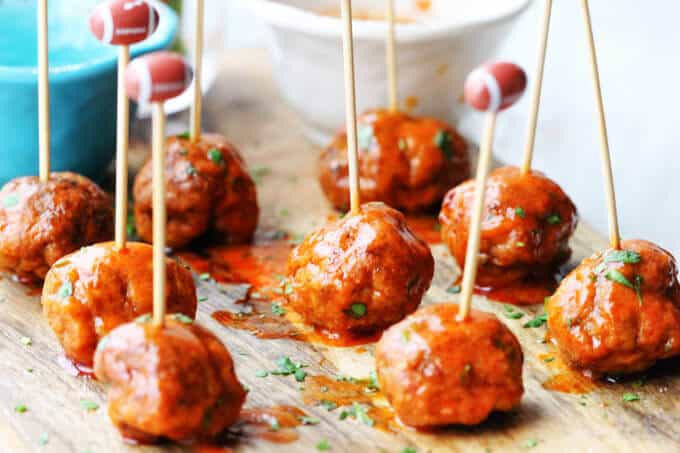 Buffalo Turkey Meatballs are a perfect appetizer for the Big Game. They're also a lighter alternative to a traditional chicken buffalo wings, not only because they have less fat, but also because they're baked, not fried. Not to mention they're also super easy to make. Buffalo Turkey Meatballs with football sticks and bowls with sauces in the back, vertical