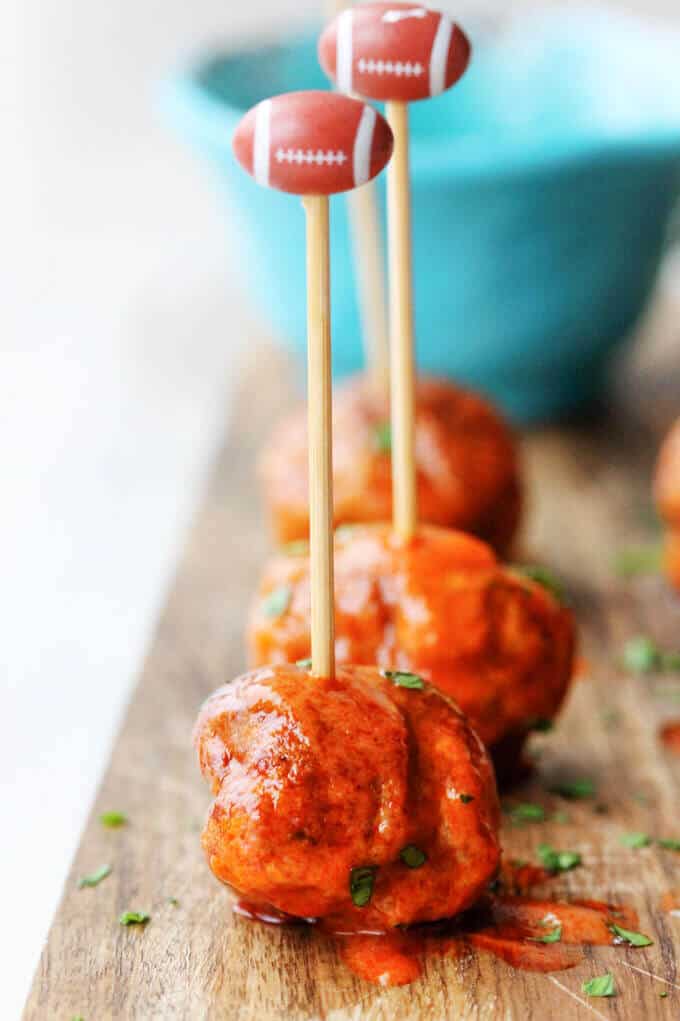 Buffalo Turkey Meatballs are a perfect appetizer for the Big Game. They're also a lighter alternative to a traditional chicken buffalo wings, not only because they have less fat, but also because they're baked, not fried. Not to mention they're also super easy to make. Buffalo Turkey Meatballs with football sticks and blue ball in the back