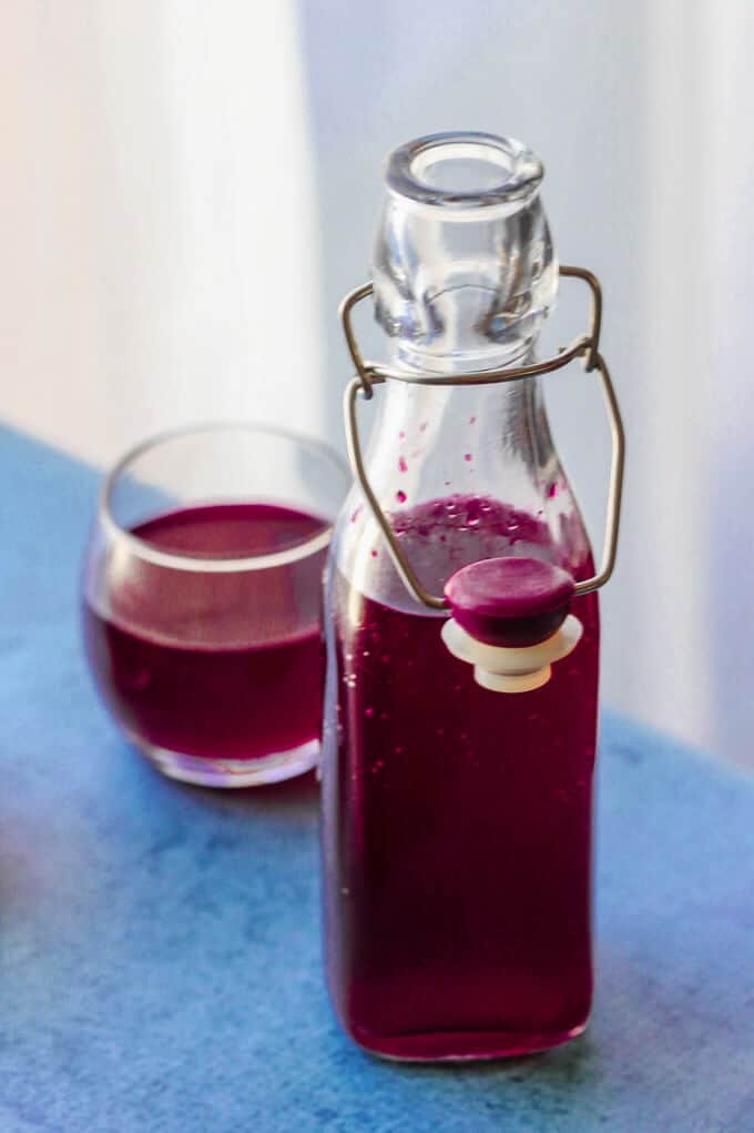 If you ever wondered how to make beet kvass, I will show you how easy it is. You just need beets, water, salt and spices. No starters, whey or bread required. How to make beet kvass - bottle on left side and glass with beet kvass on blue background