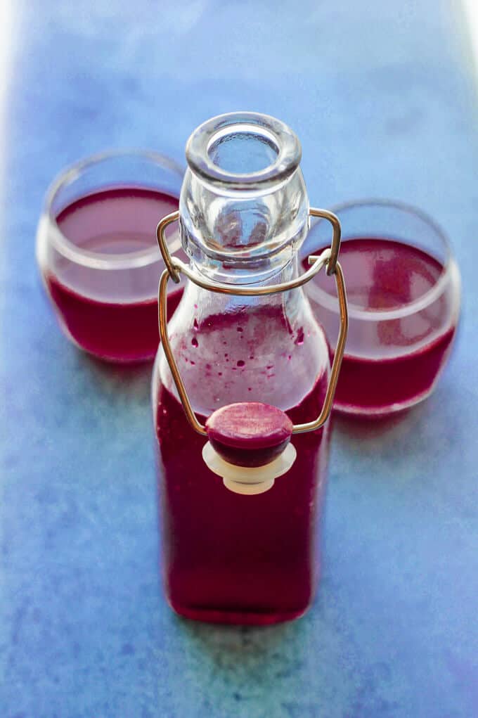 If you ever wondered how to make beet kvass, I will show you how easy it is. You just need beets, water, salt and spices. No starters, whey or bread required. How to make beet kvass - bottle and two glasses with kvass on blue background