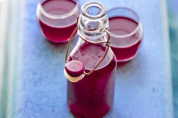 If you ever wondered how to make beet kvass, I will show you how easy it is. You just need beets, water, salt and spices. No starters, whey or bread required. How to make beet kvass - bottle and two glasses with beet kvass ion blue background, vertical