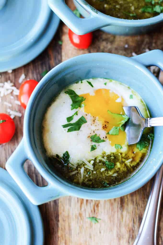 Baked eggs with tomatoes and pesto in blue ramekin with fork breaking the yolk.