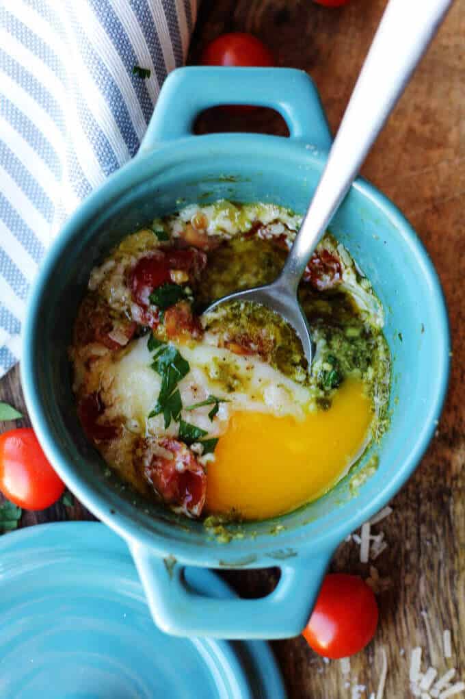 These Baked Eggs with Tomatoes and Pesto can be added to your ketogenic breakfast menu if you are looking for low carb recipes. It's super quick, delicious, naturally low in carbs and packed full of healthy fats. baked eggs with tomatoes and pesto with spoon inside the ramekin