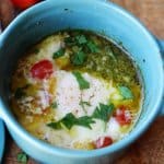 baked eggs with tomatoes and pesto in blue ramekin, horizontal shot