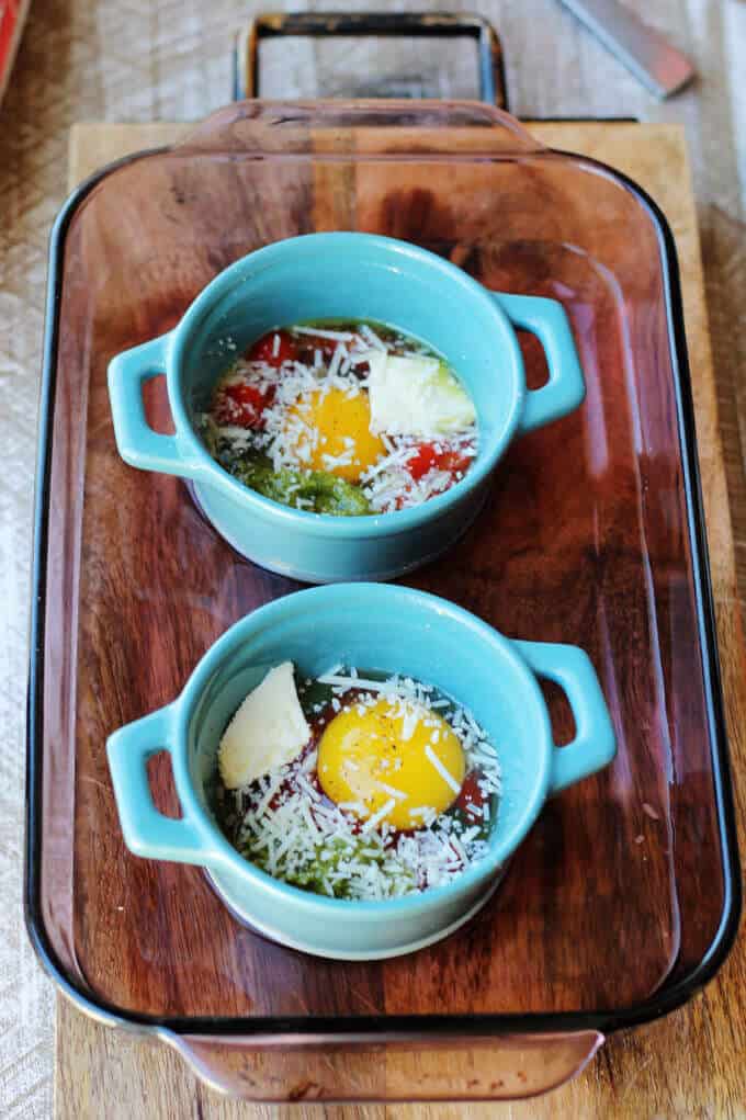 These Baked Eggs with Tomatoes and Pesto can be added to your ketogenic breakfast menu if you are looking for low carb recipes. It's super quick, delicious, naturally low in carbs and packed full of healthy fats. ramekins with cracked eggs in baking dish