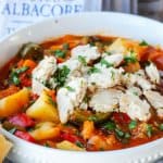 Spanish style tuna stew in a white bowl with spoon and bread on a side