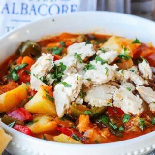 Spanish style tuna stew in a white bowl with spoon and bread on a side