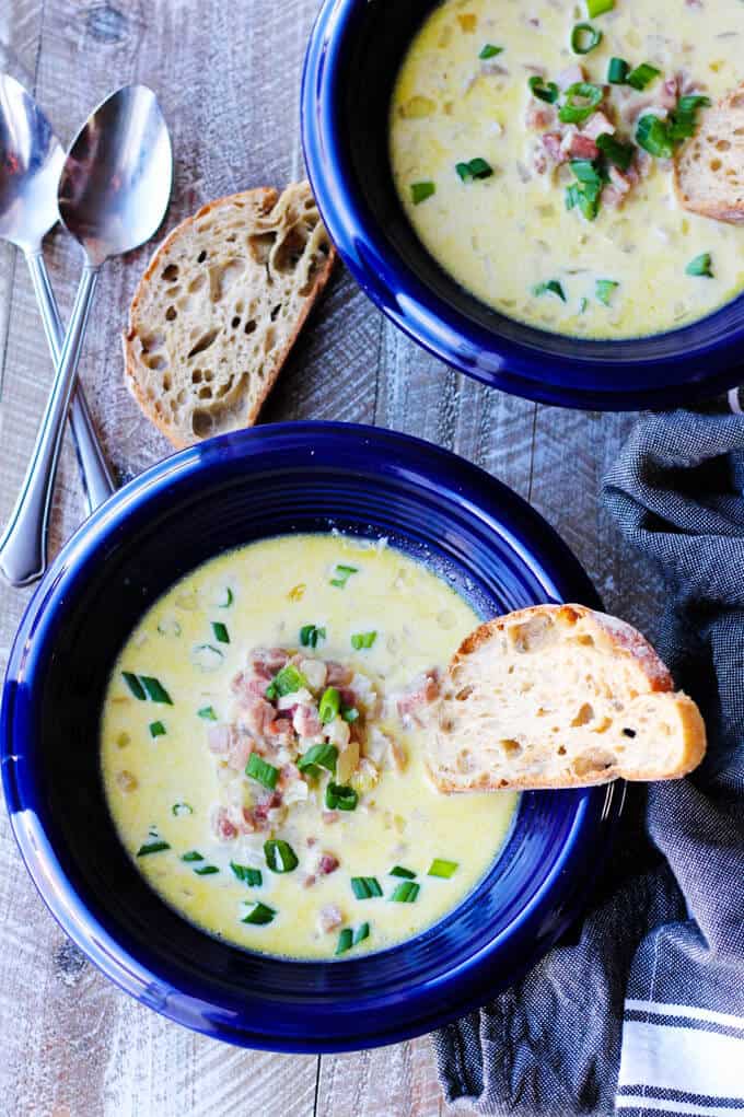 ham and cheese soup in blue bowls with toast inside and spoons on a side, overhead shot