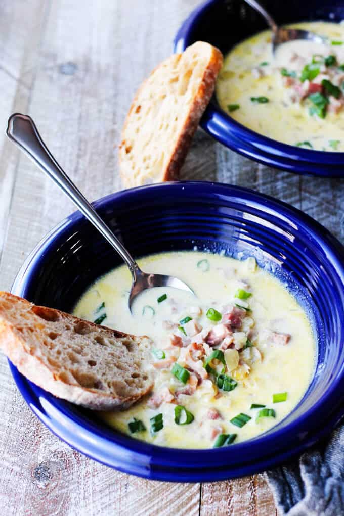 This Ham and Cheese Soup with White Wine and Gruyere is yet another recipe to show you how easily you can repurpose your leftover ham. This soup is rich and decadent, and it will keep your loved ones coming back for seconds...guaranteed. ham and cheese soup in blue bowls with scallions and bread and spoon in the bowl