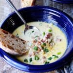 ham and cheese soup in blue bowl with scallion, bread and spoon inside, vertical shot