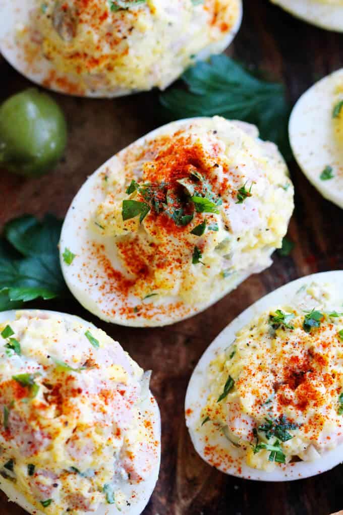 Stuffed Eggs with Ham & Cheese, sprinkled with a dash of Spanish Smoked Paprika, are super meaty, cheesy and satisfying. The subtle heat from the smoked paprika marries everything together to create a perfect egg bite. These are a MUST for your Easter table stuffed eggs on a board with olives in the back