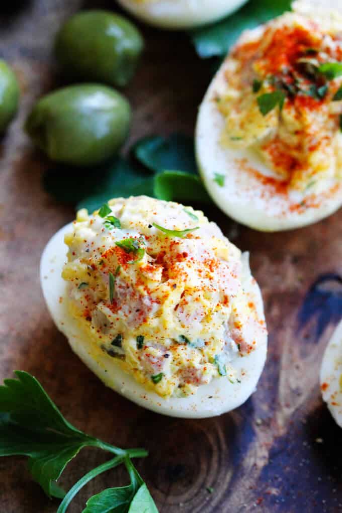 Stuffed Eggs with Ham & Cheese, sprinkled with a dash of Spanish Smoked Paprika, are super meaty, cheesy and satisfying. The subtle heat from the smoked paprika marries everything together to create a perfect egg bite. These are a MUST for your Easter table stuffed eggs on a board with olives in the back