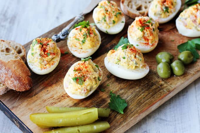 Stuffed Eggs with Ham & Cheese, sprinkled with a dash of Spanish Smoked Paprika, are super meaty, cheesy and satisfying. The subtle heat from the smoked paprika marries everything together to create a perfect egg bite. These are a MUST for your Easter table stuffed eggs on a board with bread, olives and pickles, diagonal lay out