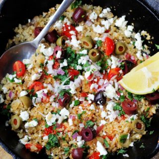 Fried riced cauliflower with Mediterranean twist in a skillet with spoon and lemon