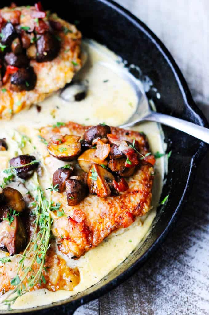 Pork chops in white wine cream sauce with mushrooms and bacon in a pan with a spoon in the sauce