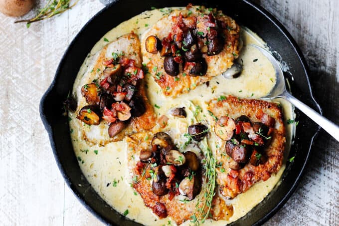 Pork chops in creamy white wine sauce with mushrooms and bacon in a pan, overhead, horizontal shot