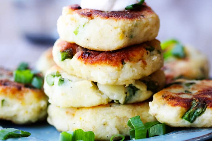 This recipe for Potato Cutlets with Asparagus is a keeper. In fact, the ease of preparation, coupled with deliciousness of the dish, might catapult this one into heavy rotation. Preparation just requires a few steps that and, again, the taste is amazing. Potatoes with asparagus - fried to perfection - and served with a dollop of sour cream and scallions. And while there are no breadcrumbs involved, they still achieve crispy and golden brown crust. Potato cutlets stacked up on a plate with green onions around; horizontal shot