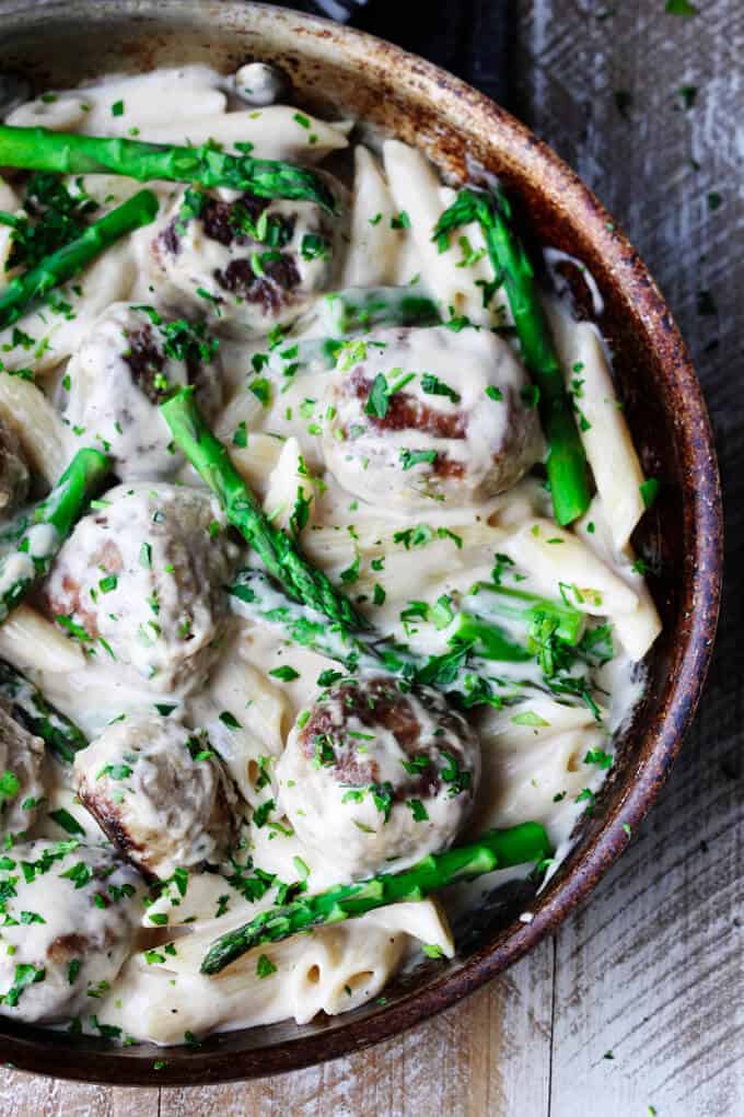 This Turkey Meatballs Alfredo Pasta with Asparagus is a perfect midweek dinner, for nights when you're short on time but still want to make your family a hearty meal. It comes together quickly and incorporates a store-bought Alfredo sauce shortcut. turkey meatballs and asparagus in creamy Alfredo sauce in a frying pan on a board