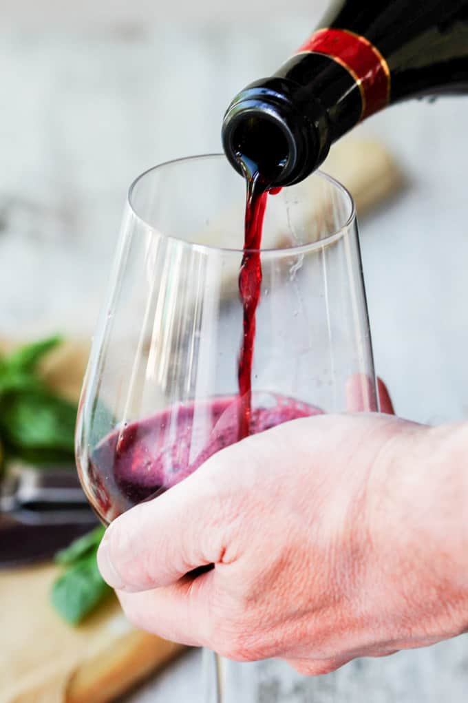 Hand holding a wine glass with pouring red wine