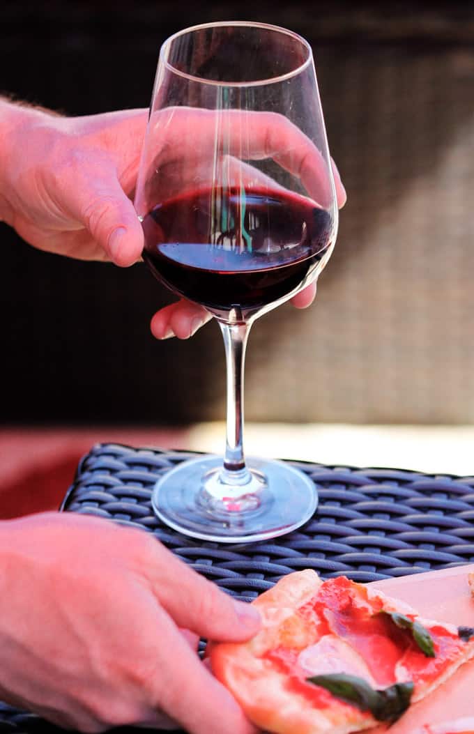 Hands holding red wine and slice of pizza