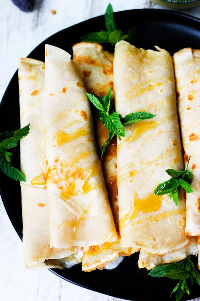 These Apple Sauce Crepes with Honey Ricotta are made with cinnamon crepes, North Coast Organic Apple Sauce, organic ricotta and raw honey. These crepes are super delicious and healthy at the same time. A perfect option for a school lunch or even an afternoon snack. Apple Sauce Crepes with Honey Ricotta rolled on a black plate