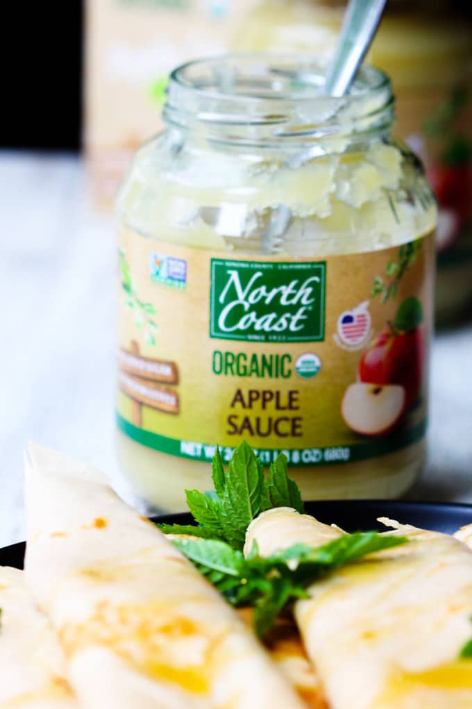 These Apple Sauce Crepes with Honey Ricotta are made with cinnamon crepes, North Coast Organic Apple Sauce, organic ricotta and raw honey. These crepes are super delicious and healthy at the same time. A perfect option for a school lunch or even an afternoon snack. Apple sauce in a jar with a spoon and crepes on a plate