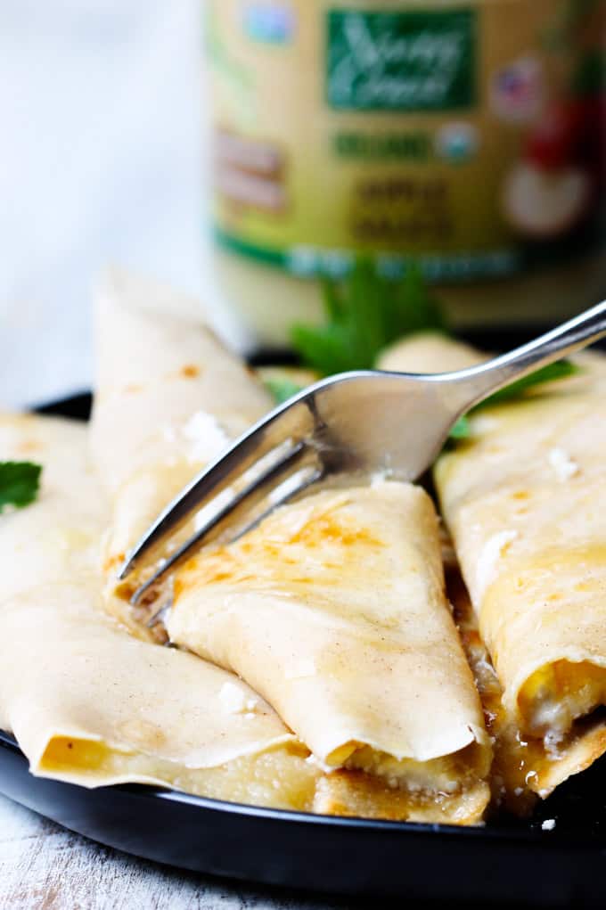 These Apple Sauce Crepes with Honey Ricotta are made with cinnamon crepes, North Coast Organic Apple Sauce, organic ricotta and raw honey. These crepes are super delicious and healthy at the same time. A perfect option for a school lunch or even an afternoon snack. Fork cutting through Apple Sauce Crepe
