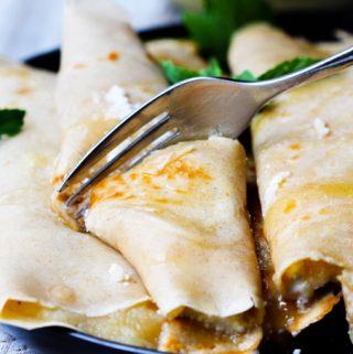 Fork cutting through crepe with apple sauce and ricotta with honey