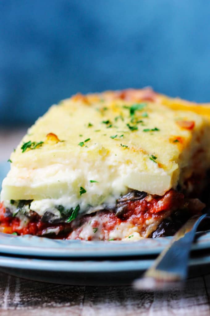 Close up shot of a piece f vegetable moussaka on a blue plate with fork