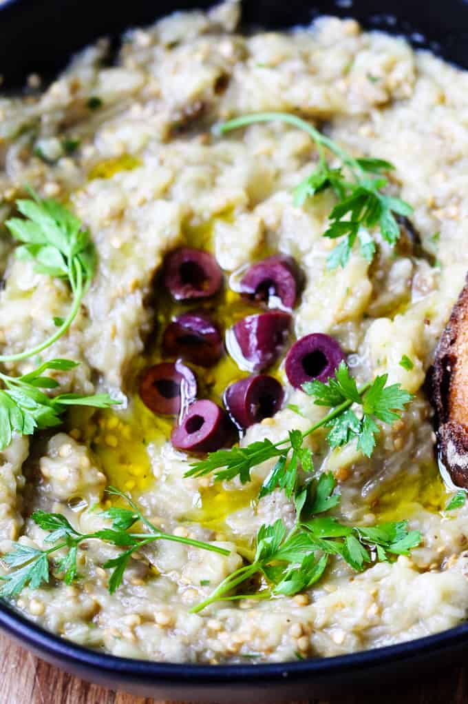 Melitzanosalata is a Greek Eggplant Dip that's made from roasted or charred eggplants, garlic, onions, olive oil, lemon juice, and parsley. It has a chunky consistency and is usually served as a mezze (appetizer) with either a pita or crusty bread. If you're looking for full emersion, you can top it with some Kalamata olives for an extra punch of flavor. Greek Eggplant Dip with olives