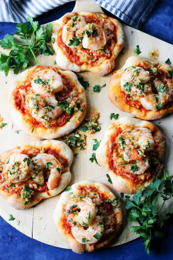 Pizzette with Garlic Shrimp and Roasted Red Pepper Pesto on a pizza peel with blue background