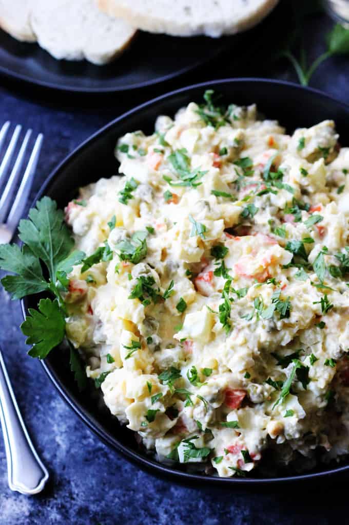 Russian salad in a black bowl with forks on a side