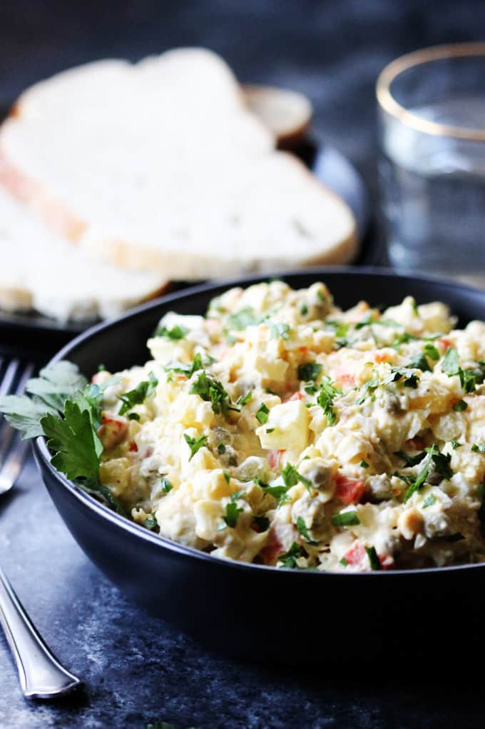 Olivier Salad in a black bowl with bread and water on a side