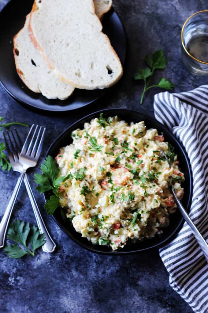Ensalada Rusa in a bowl with forks on a side, bread and kitchen towl
