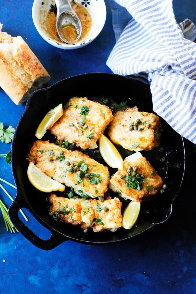 This Pan Fried Cod with Meuniere Sauce comes together in just 15 minutes! No gimmicks...it really is super simple. With just a few steps and your dinner is ready. And it will wow your kitchen patrons. Fried Cod in a skillet with brown butter lemon sauce on a side and bread